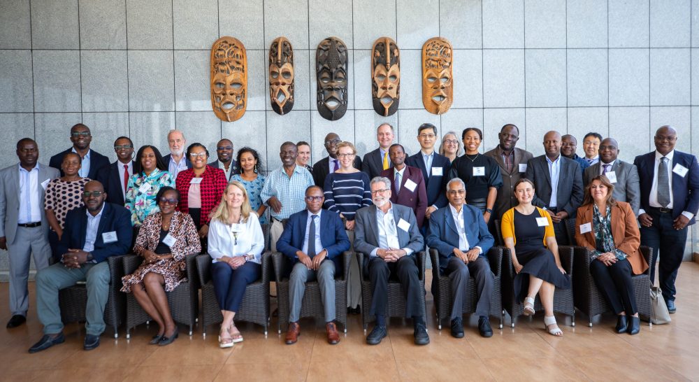 Participants of the Mectizan Expert Committee meeting posed on a balcony under a row of large wooden Malawian masks.